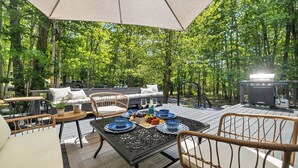 An outdoor patio with a table set for dining, surrounded by wicker furniture and a large umbrella. - Charming /Lake/Kayak/Firepit/Hot tub/Pets (Blakeslee)