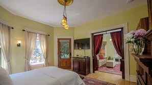 Een slaapkamer met een bed, een houten dressoir, een bureau en een stoel. Er is een raam met gordijnen, een deur en een spiegel.