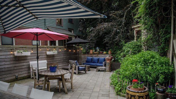 Een patio met houten meubilair, een strepenpatroon parasol en potplanten.