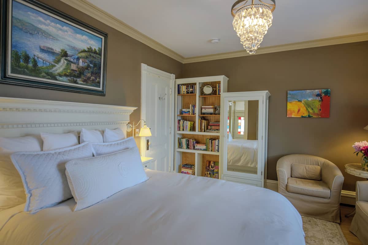 Een slaapkamer met een groot bed, een boekenkast, een stoel en een schilderij aan de muur.