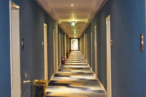 Un couloir d’hôtel avec des portes des deux côtés, une moquette à motifs et un extincteur sur le mur de gauche.
