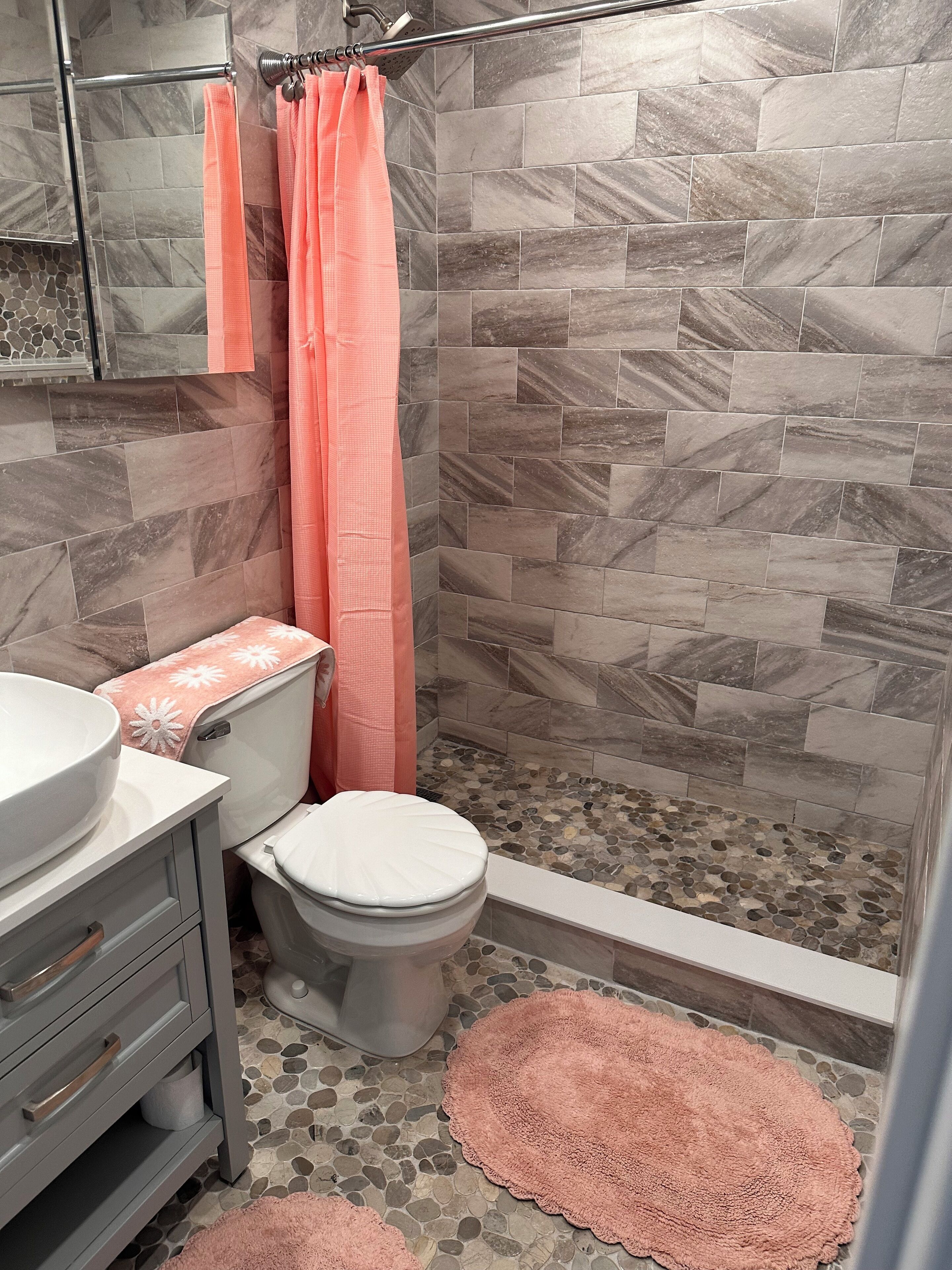 Une salle de bain équipée d’une douche, de toilettes, d’un lavabo et agrémentée d’un tapis décoratif.