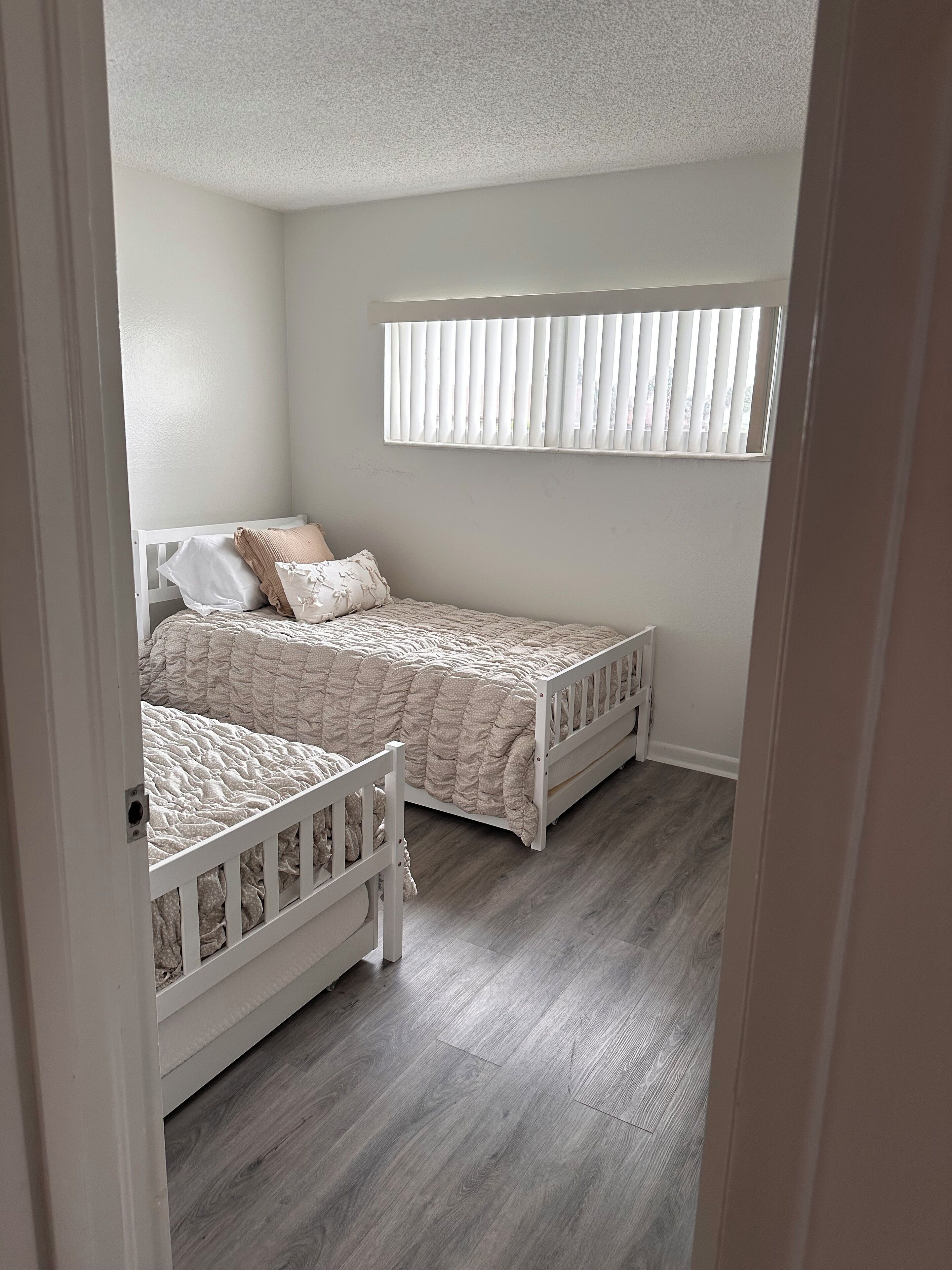 Une chambre avec deux lits simples, une fenêtre avec des stores et un plancher en bois.