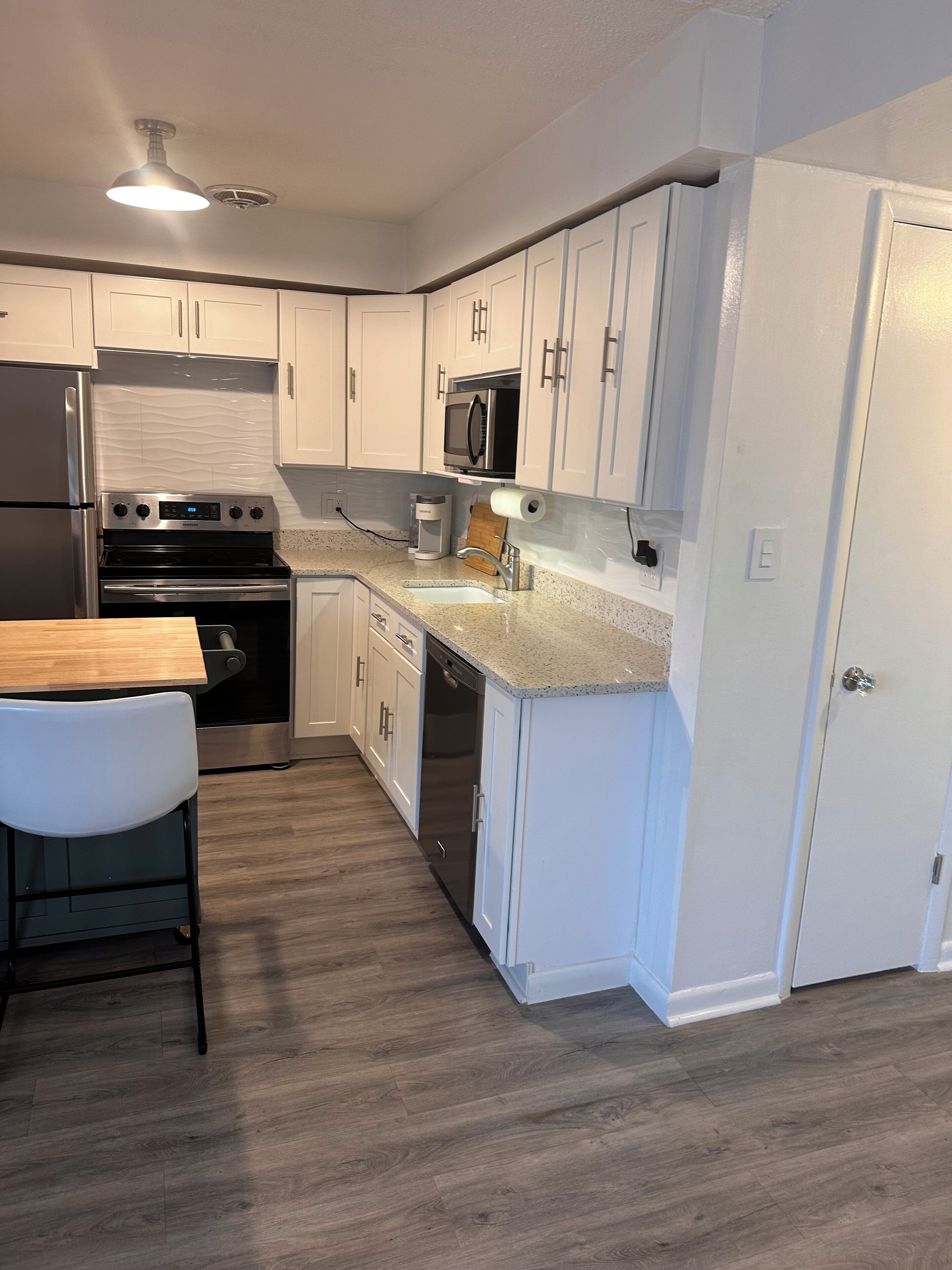 A modern kitchen with white cabinets, stainless steel appliances, and a wooden countertop.