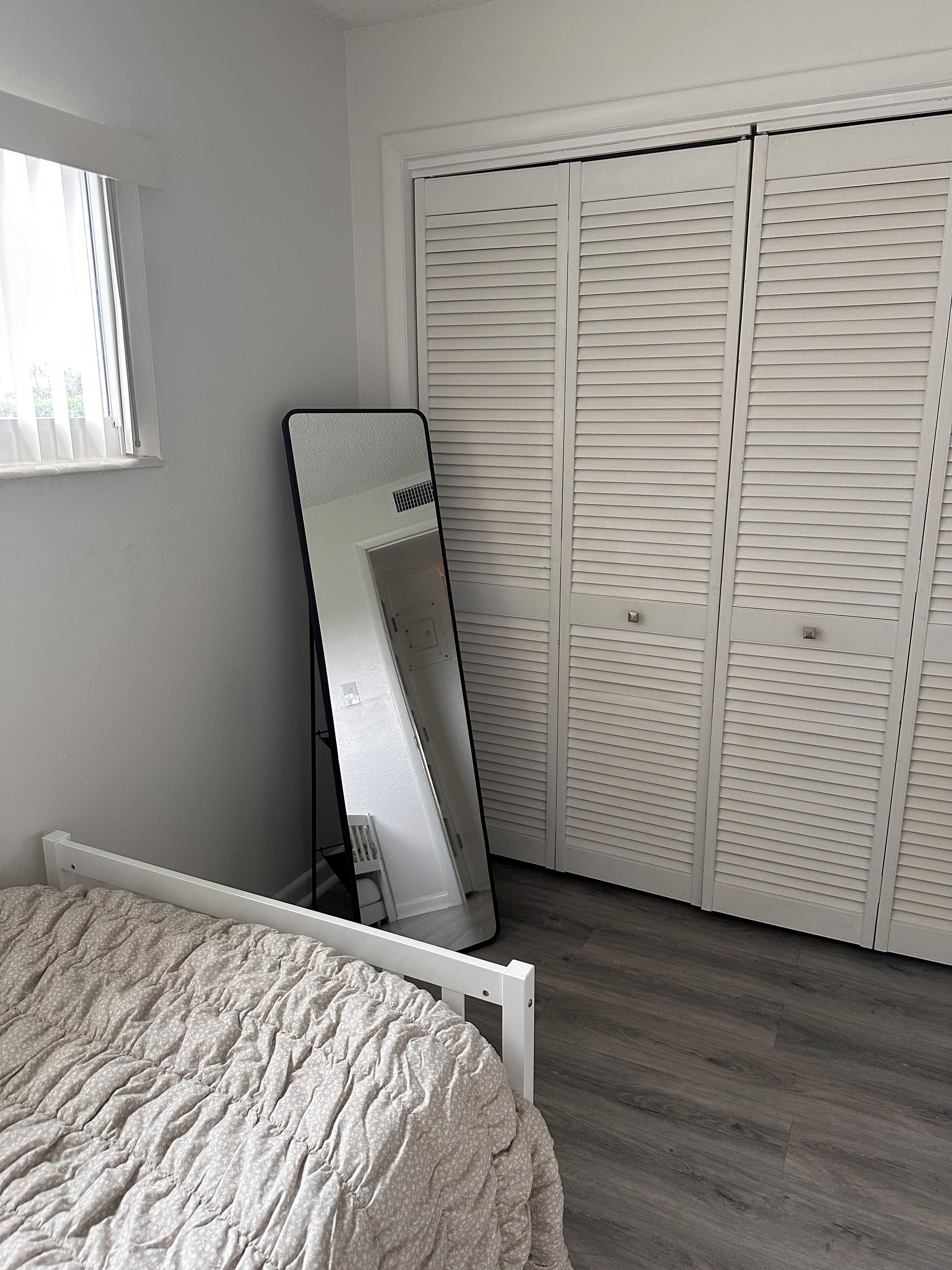 Een slaapkamer met een bed, een spiegel die tegen een muur staat en een kast met verstelbare deuren.