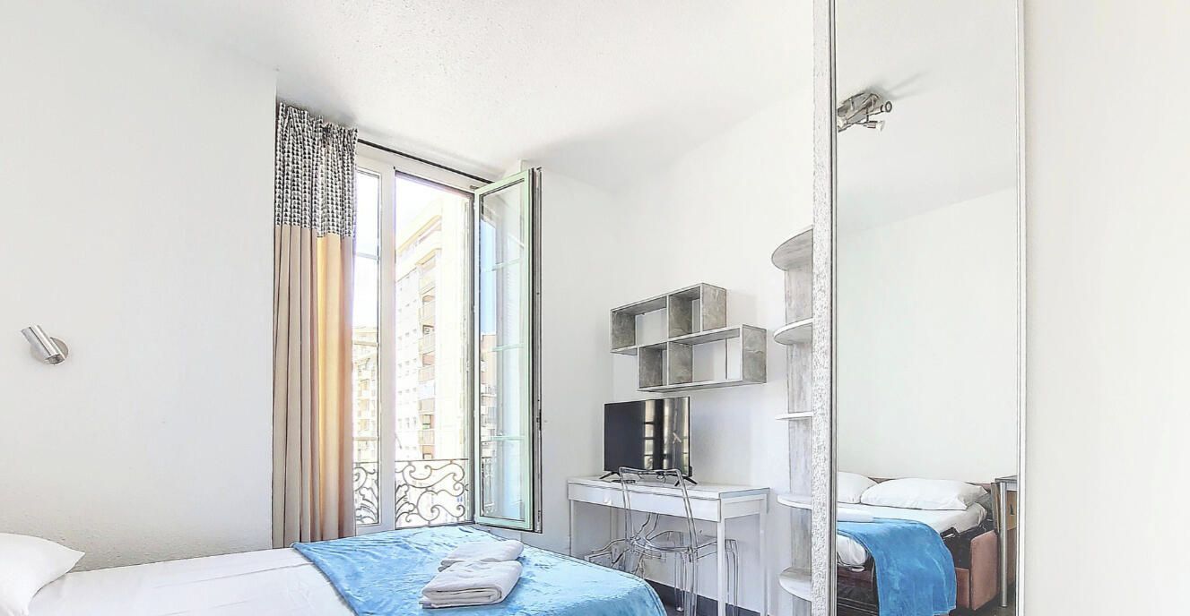 A hotel room with a bed, a desk with a computer, a TV, and a window with curtains.