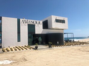 Ein modernes Gebäude mit der Aufschrift 'Vidasoul' an der Fassade, nahe einem Strand mit einer Sandfläche.