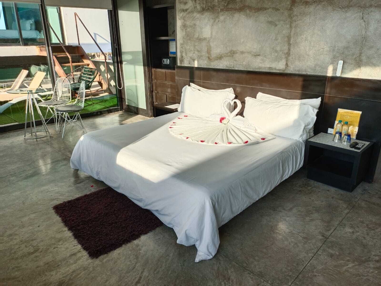 A modern hotel room with a large bed, a view of the outdoors, and a small table with a remote control.