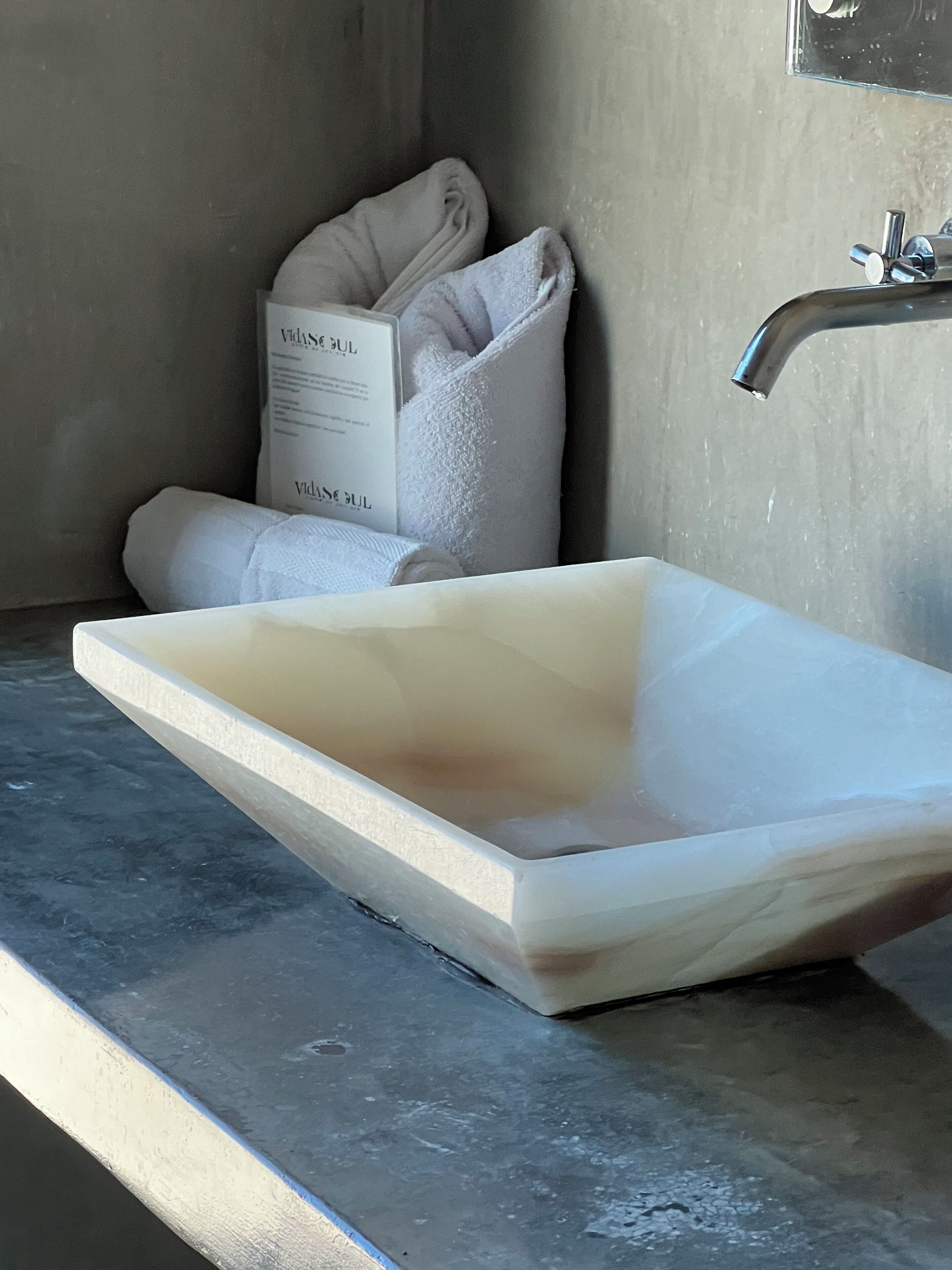 A bathroom with a rectangular sink, a towel, and a bottle of shampoo.