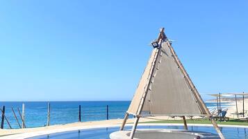 A clear blue sky, a beach, and a pool with a sailboat.