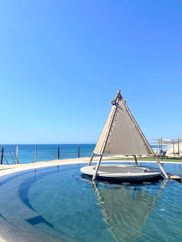 A clear blue sky, a beach, and a pool with a sailboat.