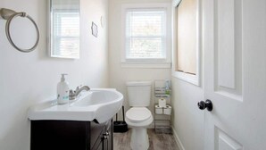 Un bany petit i funcional amb un lavabo, vàter i finestra blancs.