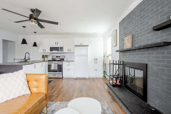 Une cuisine moderne avec des armoires blanches, une cheminée en briques noires et un ventilateur de plafond.