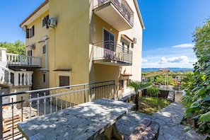 A multi-story building with balconies, a stone staircase, and a view of the landscape.