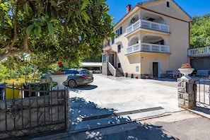 A two-story building with a balcony, a car parked in front, and a gate.