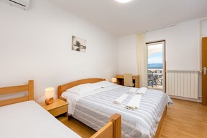 A hotel room with a bed, a desk, a chair, a lamp, a picture on the wall, and a view of the outdoors.
