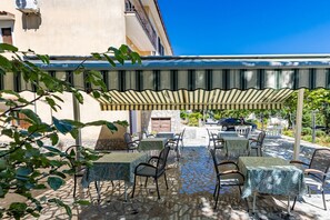 Eine Terrasse im Freien mit Tischen und Stühlen, überdacht von einem Streifenmarkisenvorzelt, und ein Steinweg, der zu einem Gebäude führt.