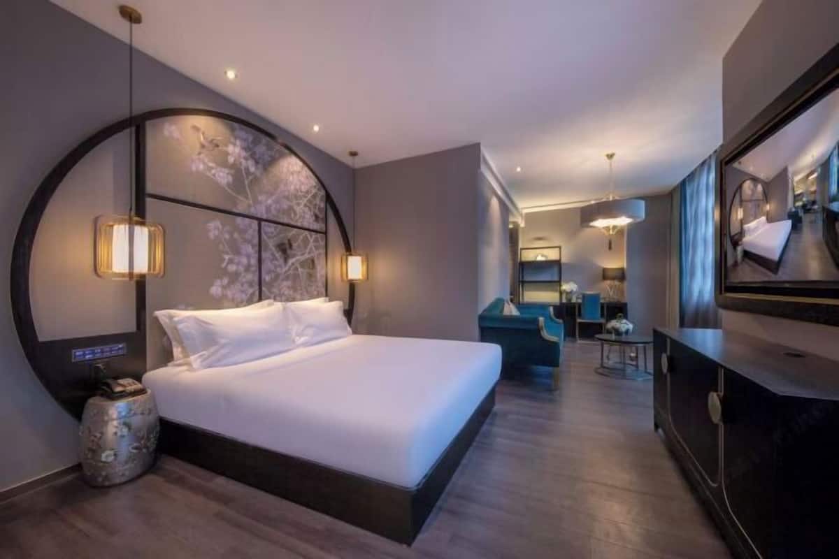 A modern hotel room with a large bed, a round wall art piece, a small round table, and a large mirror.