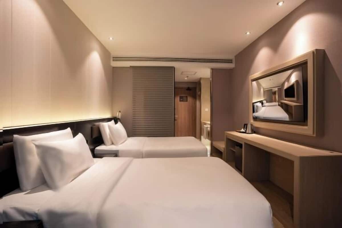 A hotel room with two beds, a large mirror, a TV, and a desk.