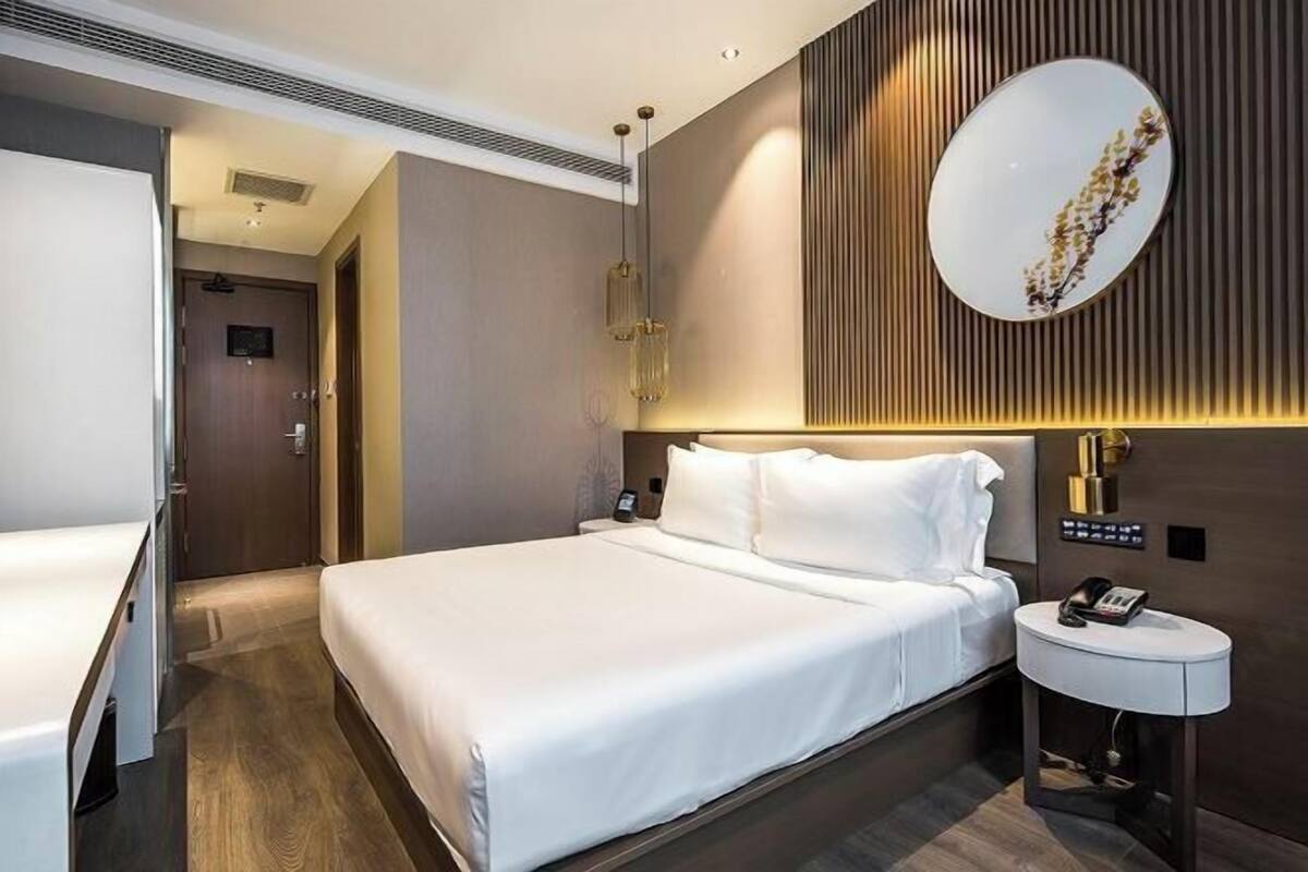 A modern hotel room with a large bed, a bedside table with a phone, and a wall-mounted mirror.