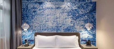 Una habitación de hotel con una cama grande, dos mesitas de noche, un papel tapiz azul con motivos y dos lámparas de pared.
