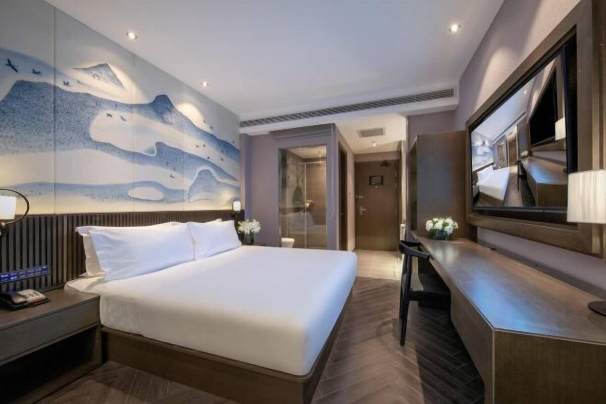 A modern hotel room with a large bed, a desk, and a wall mural.