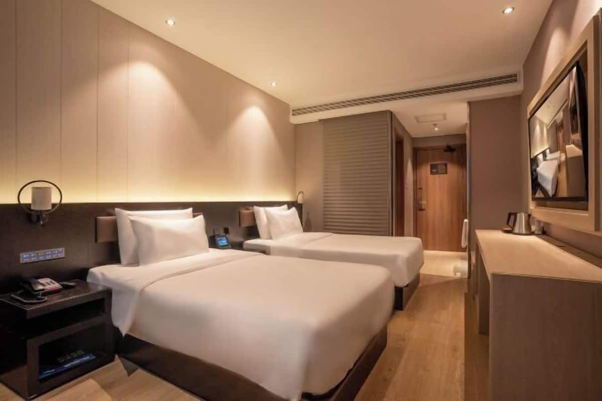A hotel room with two beds, a desk, a nightstand, a mirror, and a door leading to another room.