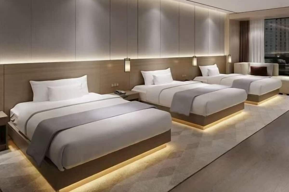 A modern hotel room with three beds, a large window, and a city view.