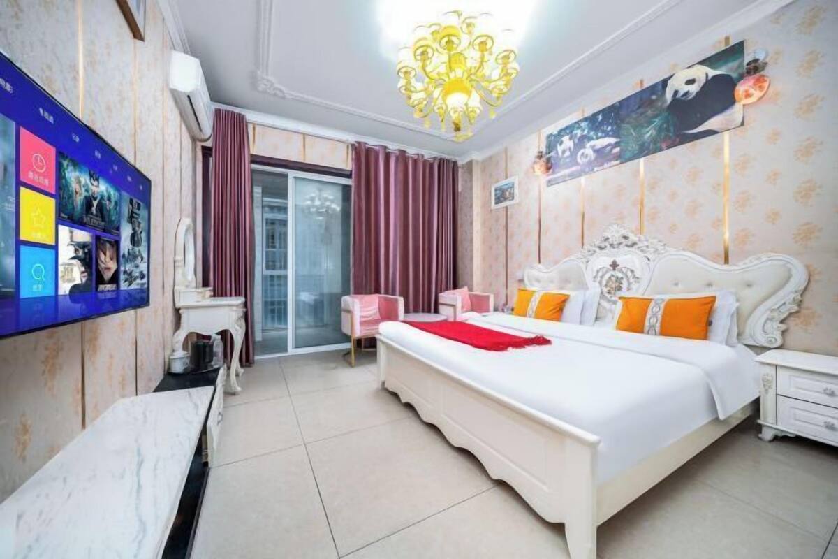 A bedroom with a large bed, a TV mounted on the wall, a chandelier, and a sliding glass door.