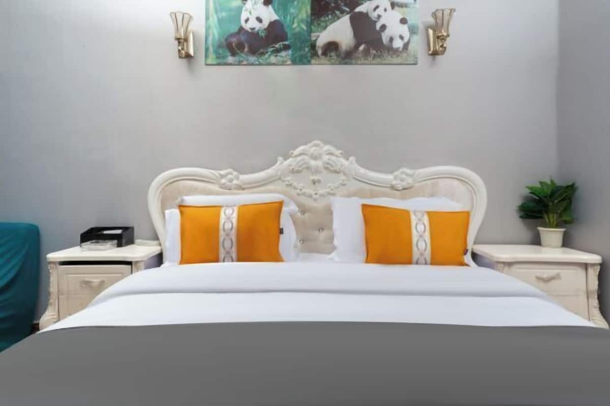 A neatly made bed with white and orange bedding, a white ornate headboard, and two bedside tables with lamps.