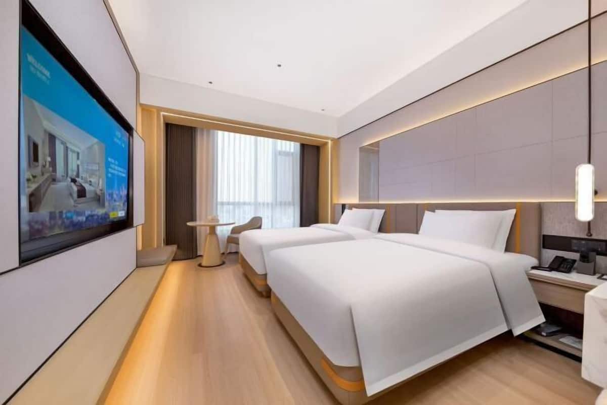 A modern hotel room with two beds, a TV, a desk, and a window with curtains.