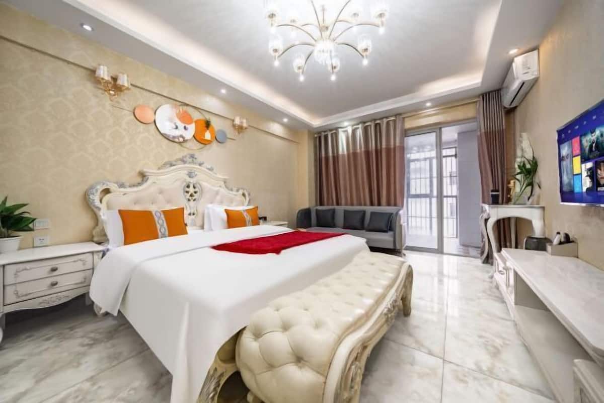 A hotel room with a large bed, a sofa, a desk, and a chandelier.