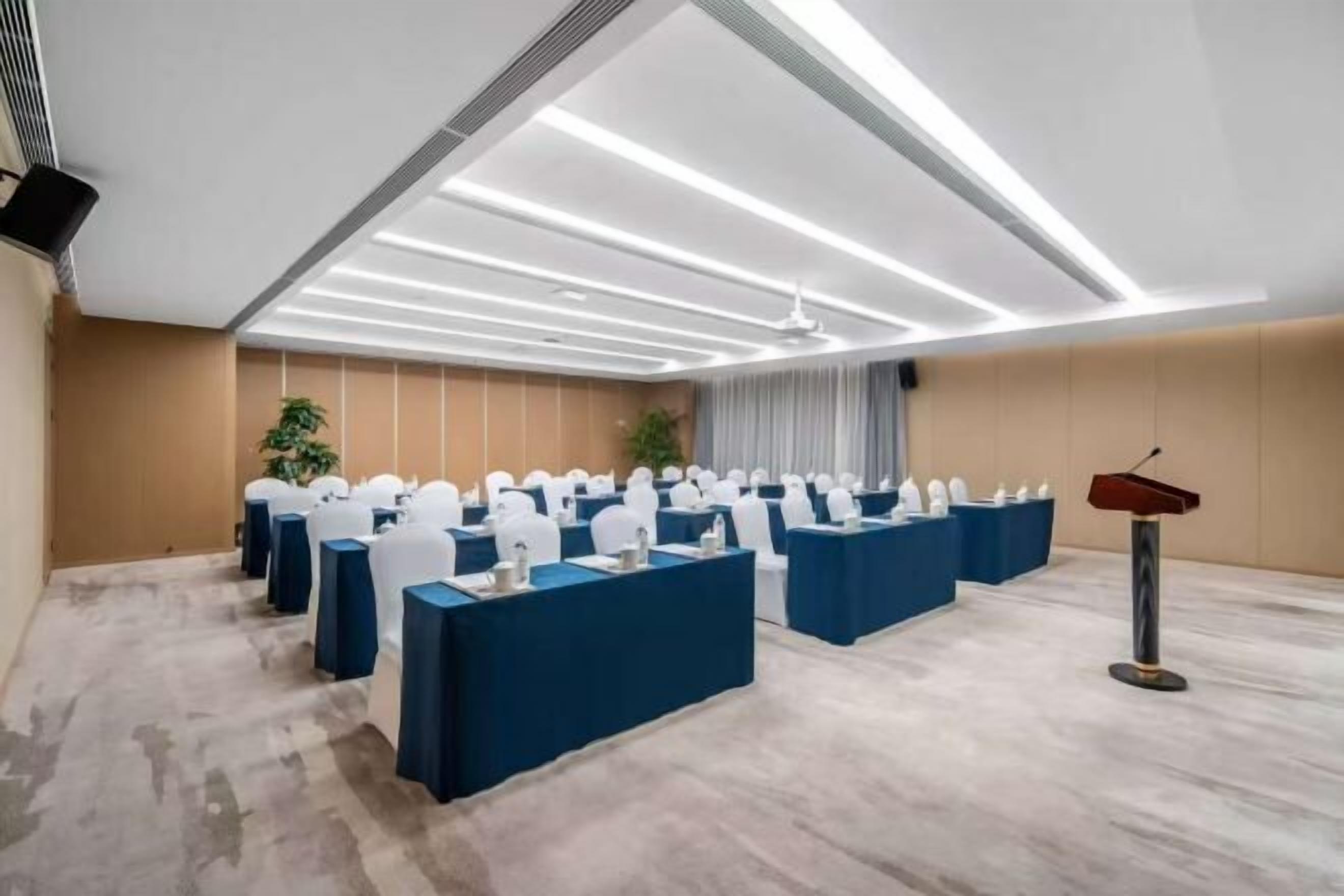 A conference room with rows of tables, a podium, and ceiling lights.