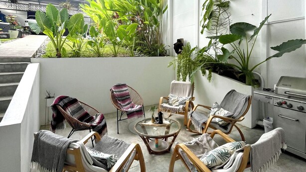 Un patio moderno al aire libre con zona de estar, una parrilla y abundante vegetación.