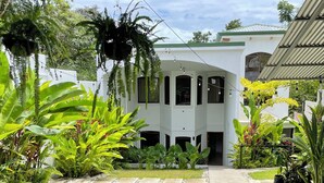 Un edificio blanco con un acceso cubierto y un jardín con diversas plantas.