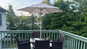 Une terrasse avec une table et des chaises, un grand parasol et une rambarde verte.