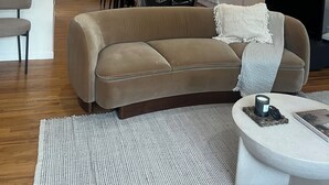 Un salon avec un canapé beige, une table basse et un téléviseur. On y trouve également une table à manger avec des chaises et un lustre au-dessus.