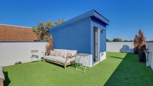Eine Dachterrasse mit einem blauen Gebäude, einem weißen Sofa und einem kleinen Tisch.
