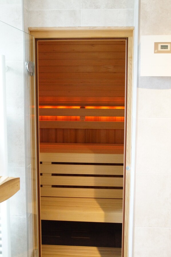 A sauna with wooden benches and a glass door, set against a tiled wall. - Spacious and luxurious wellness villa in Noordwijk with large private garden (Noordwijk)