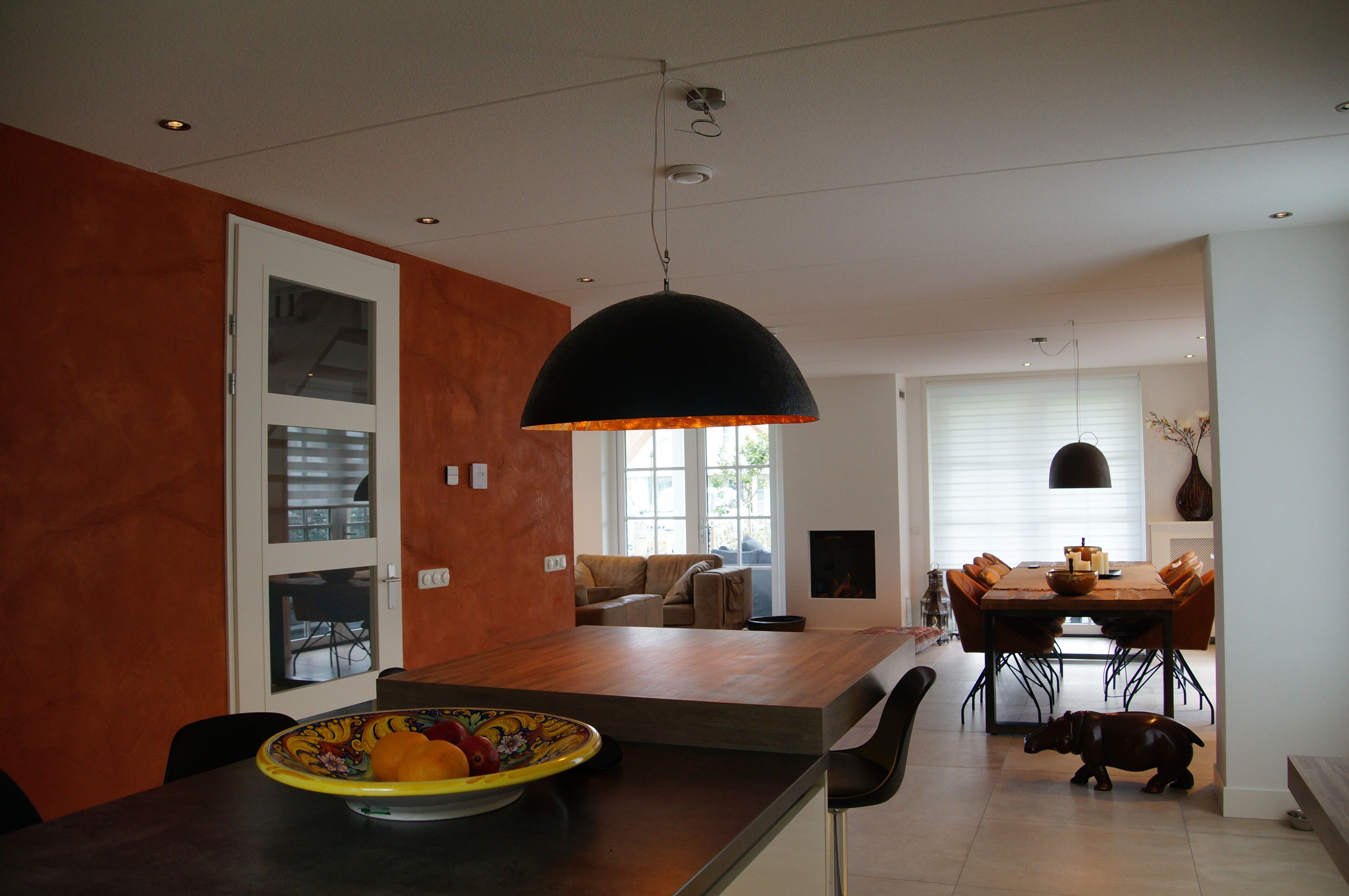 A modern kitchen with a large island, a dining area with a wooden table and chairs, and a living room with a sofa and a fireplace.