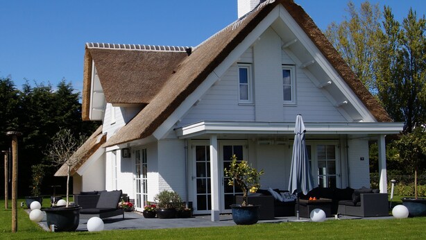 A white house with a steeply pitched roof, a covered porch, and outdoor seating.