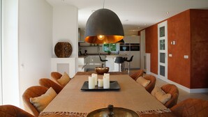 A modern dining area with a long table, multiple chairs, and a central light fixture.