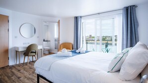 Habitación de hotel con cama, escritorio, silla, baño y balcón con vistas.