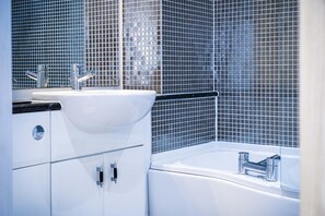 Ein modernes Badezimmer mit einem weißen Waschbecken, Chromarmaturen und einer gefliesten Rückwand.