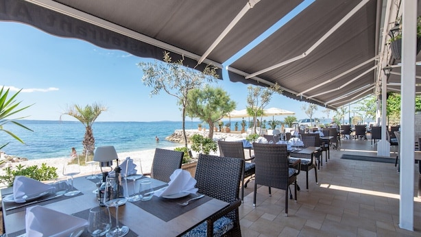 An outdoor dining area with tables set for two, overlooking a beach and the sea. - Luxury Villa David 2 heated pool 38m2 bbq Seaview (Podstrana)
