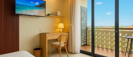 Habitación de hotel con cama, escritorio con silla, televisor en la pared, lámpara y balcón con vistas.