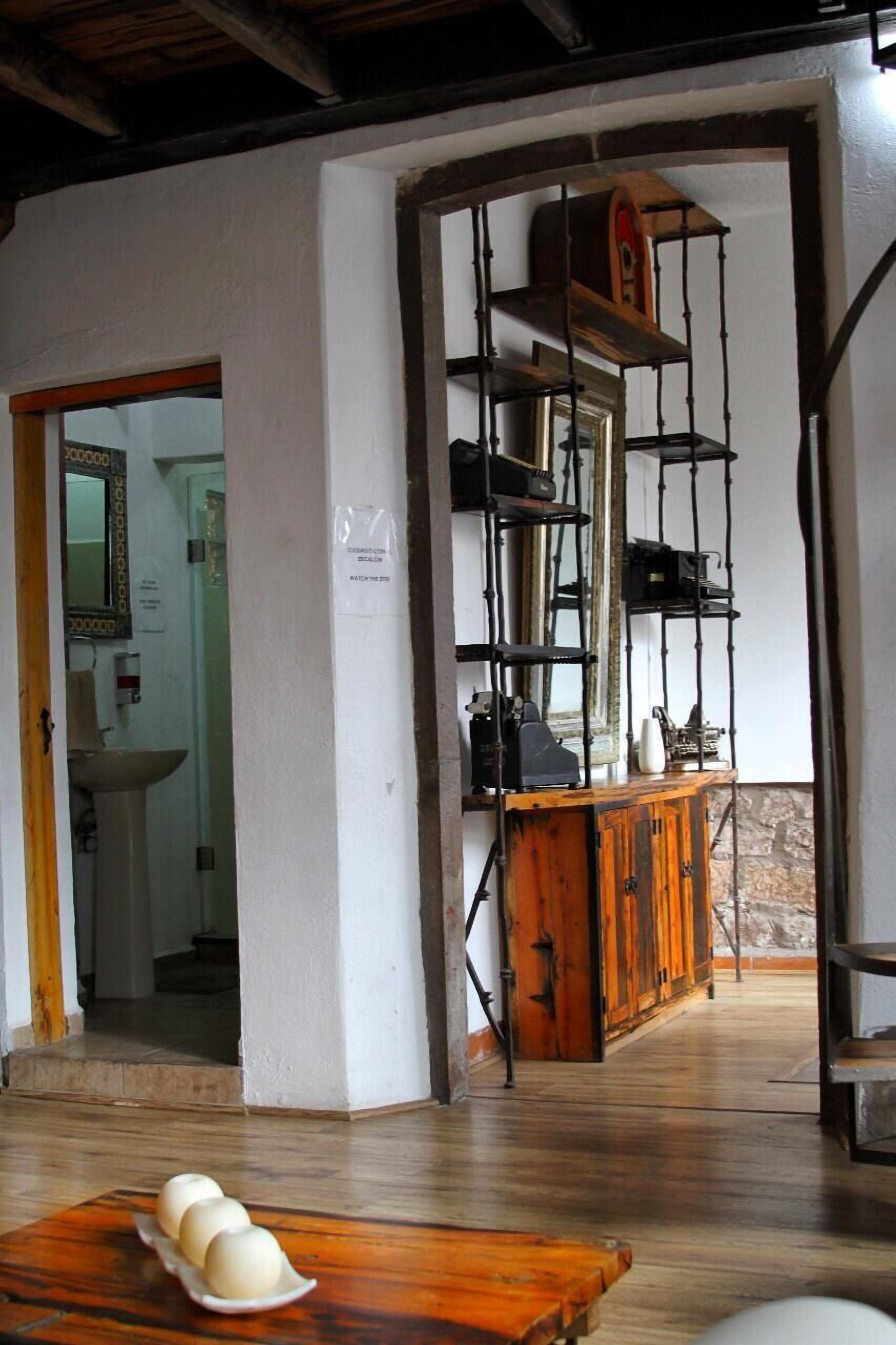 Una habitación con piso de madera, una mesa de madera con huevos, un espejo, un lavamanos y un armario con estantes.
