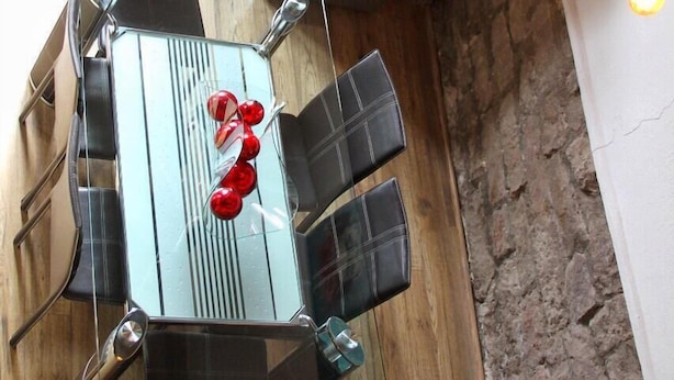 A dining area with a glass table and chairs, a decorative red object on the table, and a stone wall.