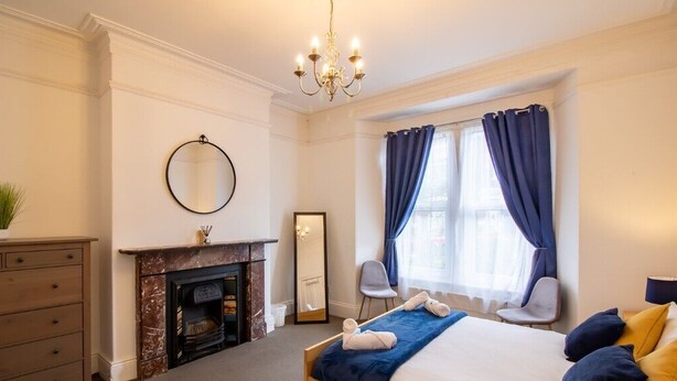 A hotel room with a bed, a fireplace, a mirror, a chair, and a window with curtains.