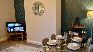 A dining area with a table set for four, a television displaying a menu, and a decorative mirror on the wall.